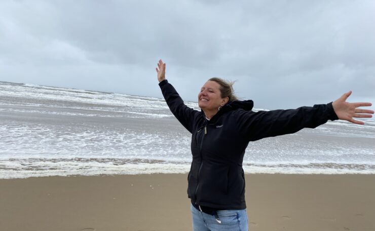 Soraya Gwynne-Evans on a beach with arms up and facing into the wind